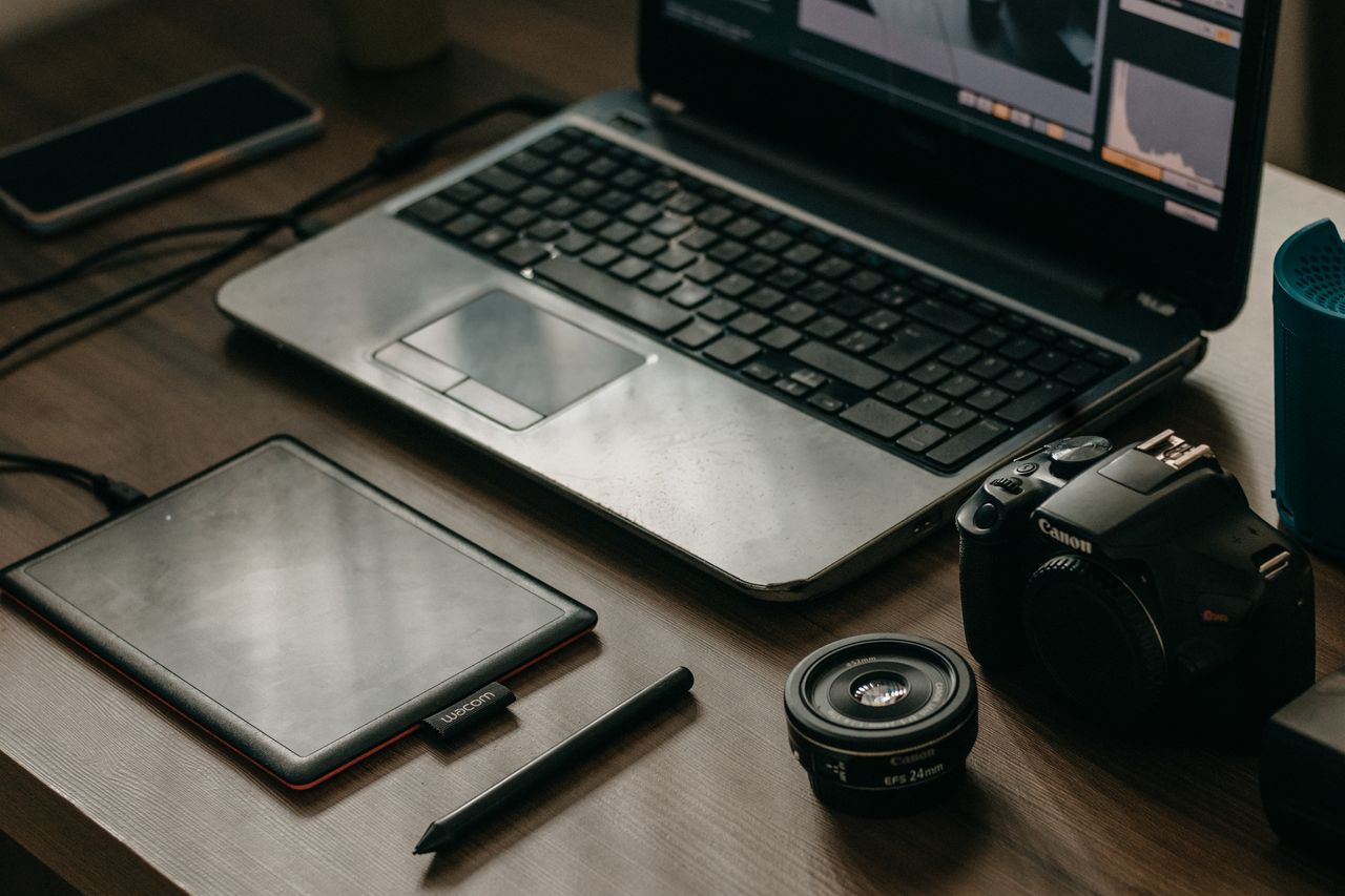 services-09 Laptop, camera, lens, and graphic tablet on a desk for digital creatives.